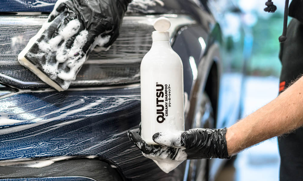 Photo of a person using a Soft99 QJUTSU Ultrasoft Sponge and Soft99 QJUTSU Creamy Shampoo to wash a car.