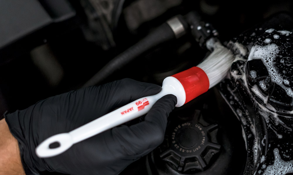 A photo of a Soft99 car care accessory Exterior Brush being used to clean an engine bay element.