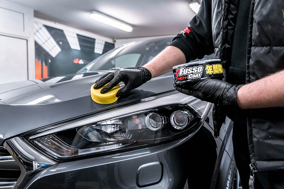 Photo of a Soft99 Fusso Coat 12 Months wax being applied on a grey car.