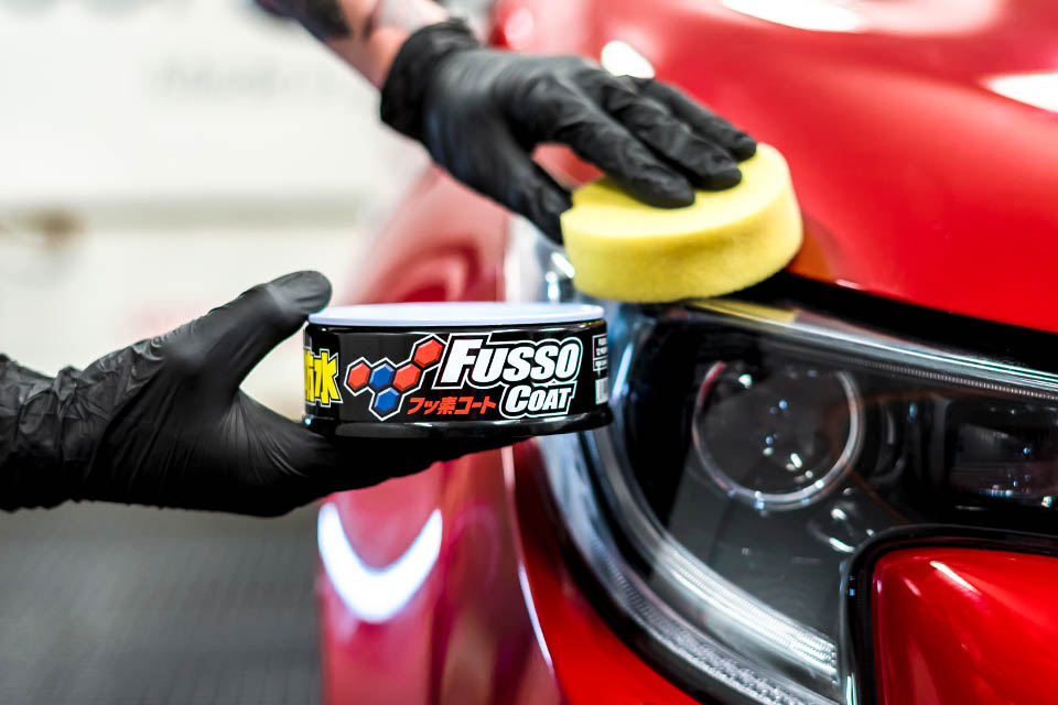 Photo of a Soft99 car care product Fusso Coat 12 Months wax being applied on a modern red car.