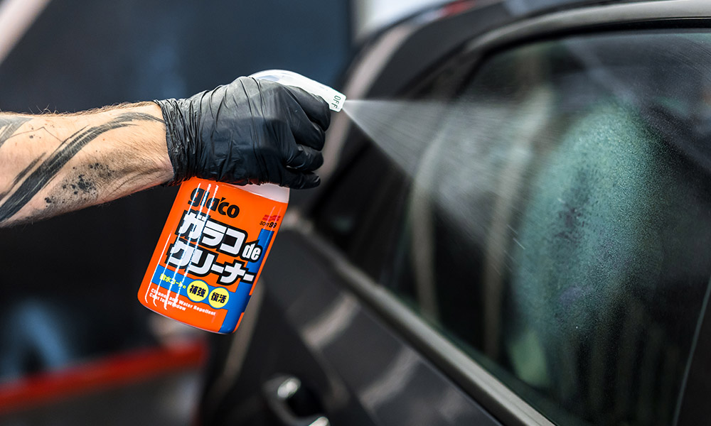 A photo of a Soft99 car care product Glaco de Cleaner being sprayed onto a car window. The product provides strong glass-cleaning porperties, while aiding and boosting the rain-repellent effect of Glaco or similar coatings.” width=