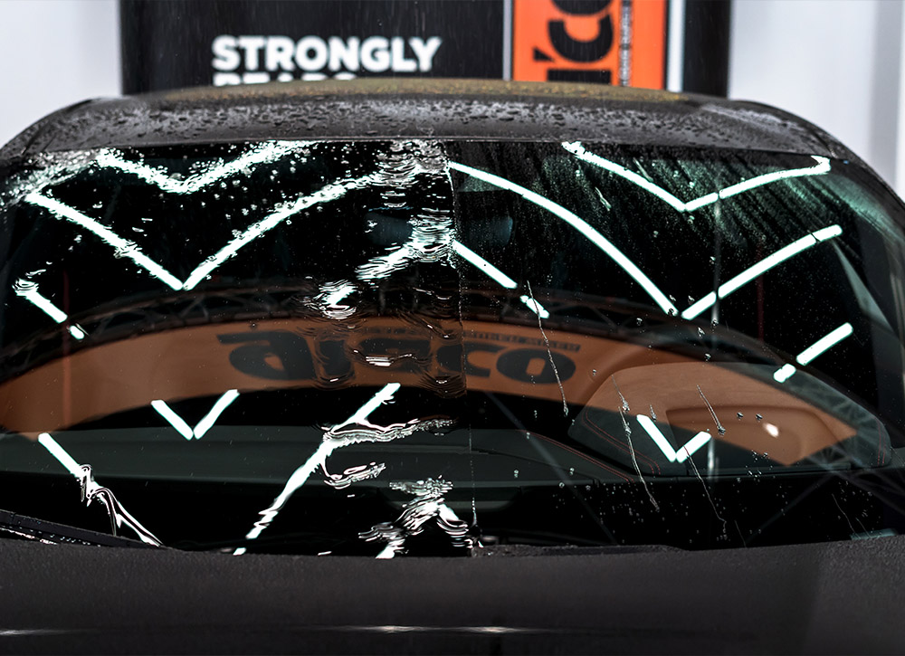 Photo of a car's windscreen, half of which was coated with water-repellent Glaco coating (on the right), the other half simply washed. Water behaviour shows visibility-enhancing water repellency of Glaco, with very limited visibility on non-coated half.
