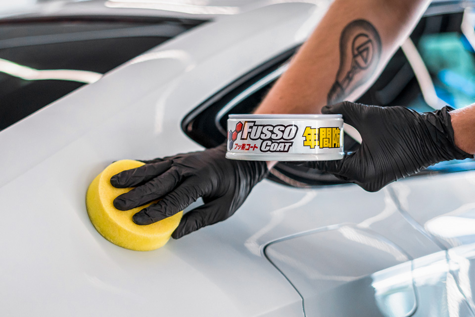 Photo of a Soft99 car wax Fusso Coat 12 Months for light paintworks being applied on a white car.