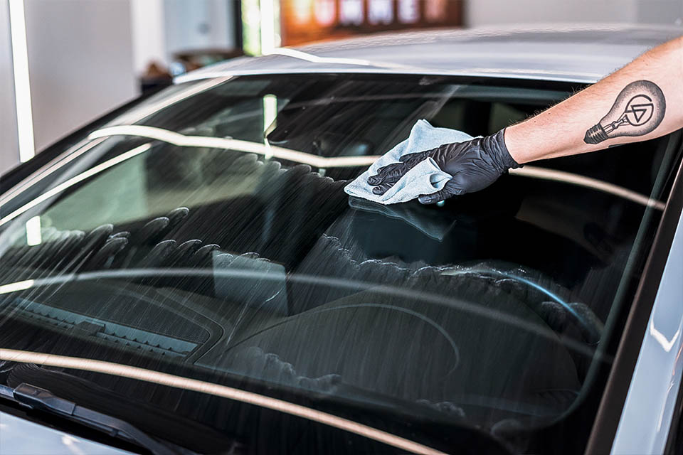 Soft99 Ultra Glaco glass coating. Photo depicts after-application polishing process, with visible white residue on glass being wiped off to create an even, water-repellent surface.